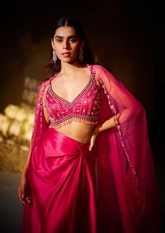 Our rose cape set presents a blend of feminine grace with its flowing skirt and hand-embellished blouse. The billowing cape adds an opulent touch to the ensemble, adorned with delicate embellishments. Pink Festive Blouse For Evening, Pink Festive Evening Blouse, Pink Silk Lehenga For Evening, Pink Georgette Evening Set, Elegant Pink Blouse With Sheer Dupatta, Evening Pink Georgette Sets, Pink Evening Set With Sheer Dupatta, Elegant Draped Pink Sets, Glamorous Pink Dress With Traditional Drape