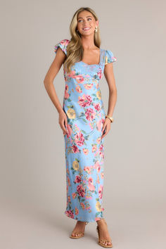 Model wearing a blue floral maxi dress. Blue Maxi Dress With Fitted Bodice For Garden Party, Spring Floral Print Maxi Dress With Fitted Bodice, Fitted Blue Floral Print Maxi Dress, Fitted Blue Maxi Dress With Floral Print, Blue Floral Maxi Dress For Party, Blue Floral Print Maxi Dress For Wedding, Fitted Maxi Dress With Floral Print For Garden Party, Blue Maxi Dress With Fitted Bodice For Spring, Spring Maxi Dress With Fitted Bodice For Wedding Guest