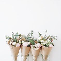 three vases filled with flowers sitting on top of a table next to a white wall