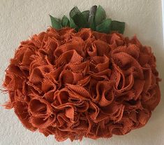 an orange wreath hanging on the wall with green leaves and burlocked fabric