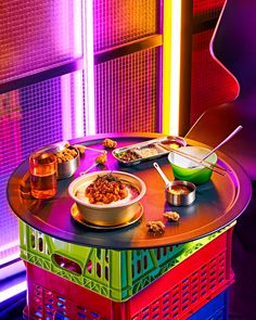 a table topped with bowls and plates of food next to a neon colored wall behind it