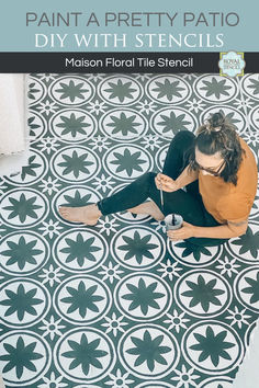 a woman sitting on the floor using a stencil to paint a tile pattern