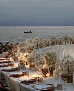 a table set up with white flowers and place settings for dinner on the water's edge