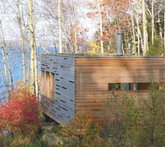 a wooden cabin sitting in the middle of a forest next to a body of water