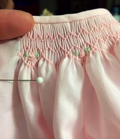 a close up of a person's hand holding a sewing needle with pink fabric