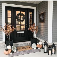 front porch decorated for fall with pumpkins, candles and wreath on the door mat