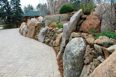 there is a rock wall along the side of this road that leads to a house