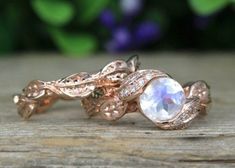 two gold rings with an opal and diamond set on top of each other, sitting on a wooden surface