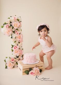 a baby girl standing in front of a cake with flowers on it and posing for the camera