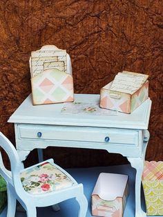 a doll house desk and chair with two boxes on top of the table next to it