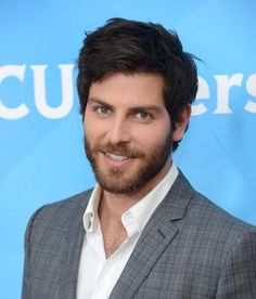 a close up of a person wearing a suit and smiling at the camera with a blue background