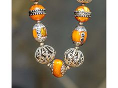 Ethnic-style 25-inch necklace made of Nepalese Copal Amber Resin and silver beads, Moroccan Filigree Silver beads, and antique Mother-of-Pearl over silver Tibetan beads. The largest silver filigree bead is 30x27 mm. The smallest mother-of-pearl beads are 8mm. Strung on a fine copper chain. Copal Amber is tree resin (not tree sap!) that is very old (expert opinions range from 1000 to 100,000 years old) but has not yet gone through the fossilization process that makes real amber (such as Baltic Am Vintage Silver Beaded Necklace For Festive Occasions, Vintage Silver Beaded Necklaces For Festive Occasions, Pearl Necklace With Round Silver Beads, Bohemian Orange Necklace For Wedding, Artisan Silver Beads Jewelry For Festivals, Artisan Silver Bead Jewelry For Festivals, Silver Beaded Temple Necklace For Festivals, Festival Silver Beaded Temple Necklace, Silver Necklaces With Polished Beads For Festival