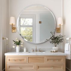 a bathroom with a large round mirror above the sink and two vases on the counter