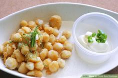 a white bowl filled with tater tots next to a small container of sour cream