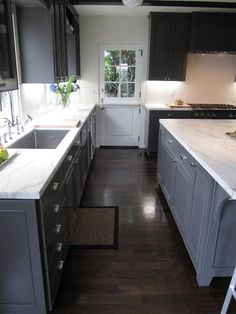 a kitchen with black cabinets and white counter tops, along with dark wood flooring