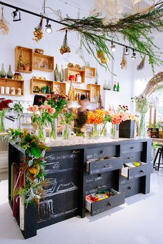 a kitchen with lots of flowers on the counter and hanging plants in vases above it