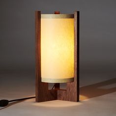 a wooden table lamp with a white light on it's side and a black cord plugged in