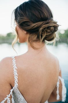 the back of a woman's dress with white lace on it and her hair in a low bun