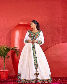 a woman standing in front of a red wall wearing a white dress with colorful patterns