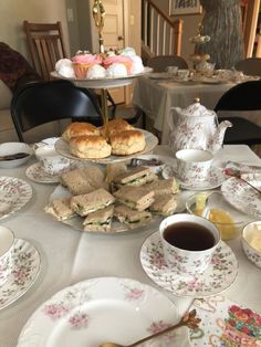 a table topped with plates and cups filled with sandwiches next to muffins on top of each other