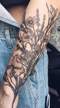 a woman's arm with flowers and leaves tattooed on the arm, in black ink