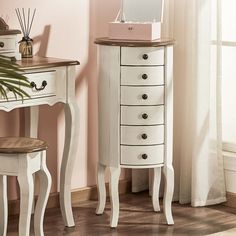 a white dresser sitting next to a mirror on top of a wooden table in front of a window