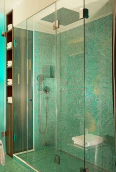 a bathroom with a glass shower door and green tiles on the walls, along with a white toilet