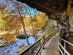 a wooden walkway leading to a river in the fall with colorful trees and rocks surrounding it