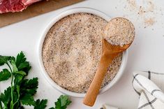 a wooden spoon sitting in a bowl next to some meat and parsley on a table