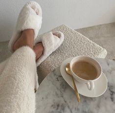 a person with their feet up on a table next to a coffee cup and saucer