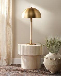 a white vase with a plant in it next to a gold lamp on a table