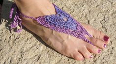 a woman's feet with purple crocheted sandals on the sand at the beach