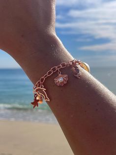 a woman's arm wearing a bracelet with charms and seashells on it