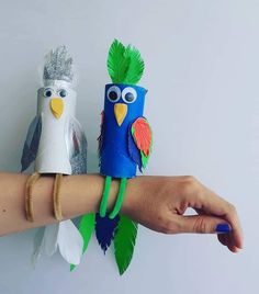 two paper birds sitting on top of each other in front of a hand with bracelets