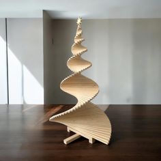 a wooden spiral christmas tree sitting on top of a hard wood floor next to a white wall