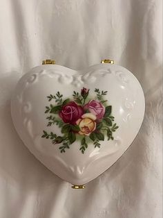 a white heart shaped box with flowers painted on the side and gold trimmings