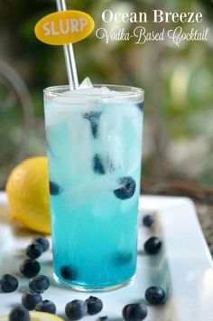 a drink with blueberries and ice on a white plate next to lemon wedges