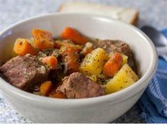 a white bowl filled with stew and carrots on top of a blue table cloth