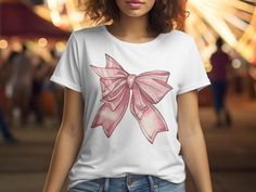 Introducing the Pink Bow Graphic T-Shirt, a charming addition to any wardrobe with its adorable pink bow design. Perfect for those who love the cute coquette aesthetic, this coquette bow shirt embodies the soft girl era with its delicate ribbon details. Ideal for girlie girls, this bow shirt is a versatile piece that pairs well with any outfit. Whether you're looking for a gift for mom, daughter, or simply treating yourself, this preppy bow t-shirt is sure to delight. Embrace the coquette vibe w Casual Summer T-shirt With Pink Bow, Casual Short Sleeve T-shirt With Pink Bow, Feminine Cotton Short Sleeve T-shirt, Feminine Pink Crew Neck T-shirt, Cute Pink T-shirt With Custom Print, Cute Cotton T-shirt With Pink Bow, Casual Cotton T-shirt With Pink Bow, Cute Summer T-shirt With Pink Bow, Pink T-shirt With Bow For Summer