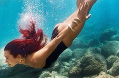 a woman with red hair is swimming in the water and holding her hands up above her head