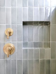 two gold faucets on the side of a white tiled shower stall in a bathroom