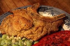 a plate topped with fried chicken and vegetables next to a slice of breaded tomato