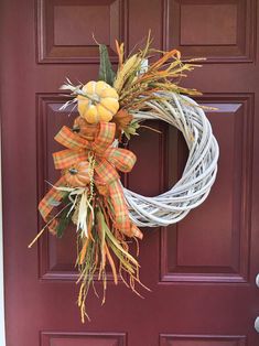 a white wreath with orange and yellow pumpkins hanging on a door