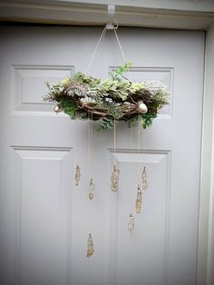 a wreath hanging on the front door with pine cones and greenery attached to it