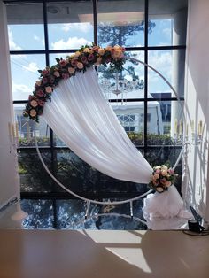 a wedding arch decorated with flowers and white draping in front of a window