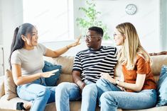 three people sitting on a couch talking to each other and pointing at something in front of them