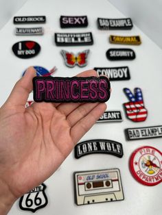 a hand holding up a sticker that says princess surrounded by various patches and badges