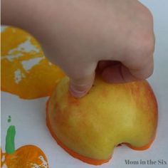 a hand is picking up an apple with oranges on the table next to it