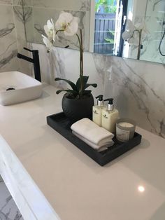 a bathroom counter with soap, toothbrushes and a flower in a vase on it