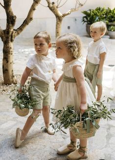 two young children standing next to each other holding baskets filled with plants and greenery